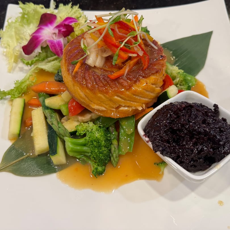 Pan-seared fish with colorful vegetables, a purple orchid, and a side of black olive tapenade.