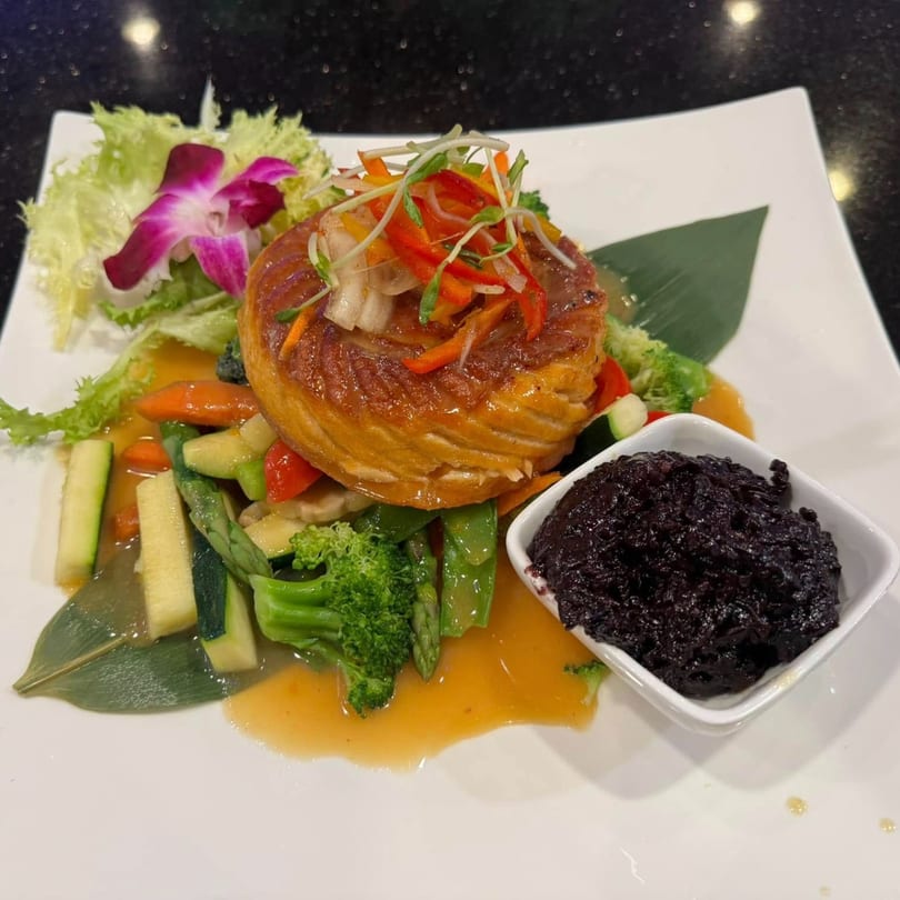 Saga Fusion's Asian-fusion dish with a golden-brown pastry, colorful vegetables, and a side of black rice.