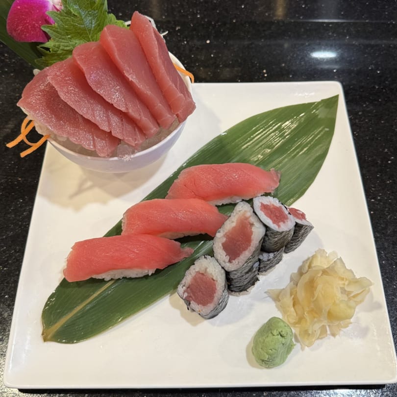 A white plate with tuna sashimi, nigiri, and maki rolls, served with ginger and wasabi.