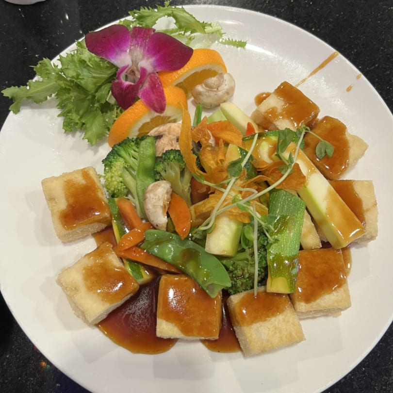 Saga Fusion's fried tofu with mixed vegetables, garnished with an orchid and orange slices.