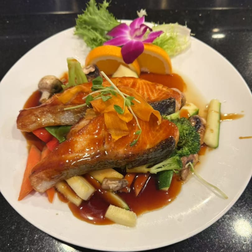 Saga Fusion's salmon teriyaki with mixed vegetables, garnished with orange slices and an orchid.