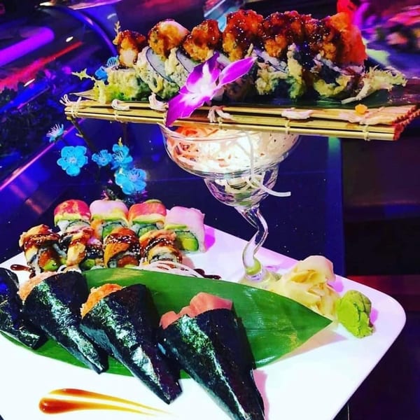 A vibrant display of Saga Fusion sushi rolls, hand rolls, and sashimi, garnished with an orchid.