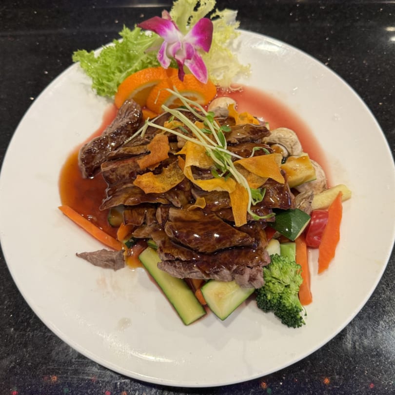 Saga Fusion's Asian-fusion beef dish with vegetables, orange slices, and an orchid on a white plate.