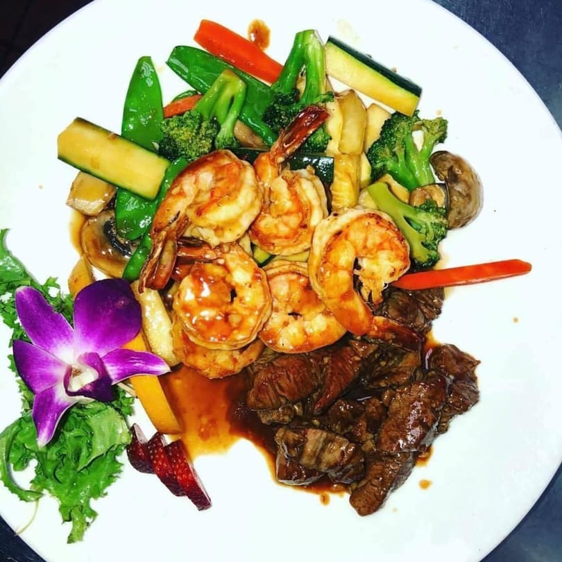 Saga Fusion's shrimp and steak entree with mixed vegetables and a purple orchid garnish.