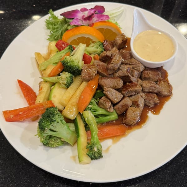 Saga Fusion's steak bites with mixed vegetables, orange slices, and a side of sauce.