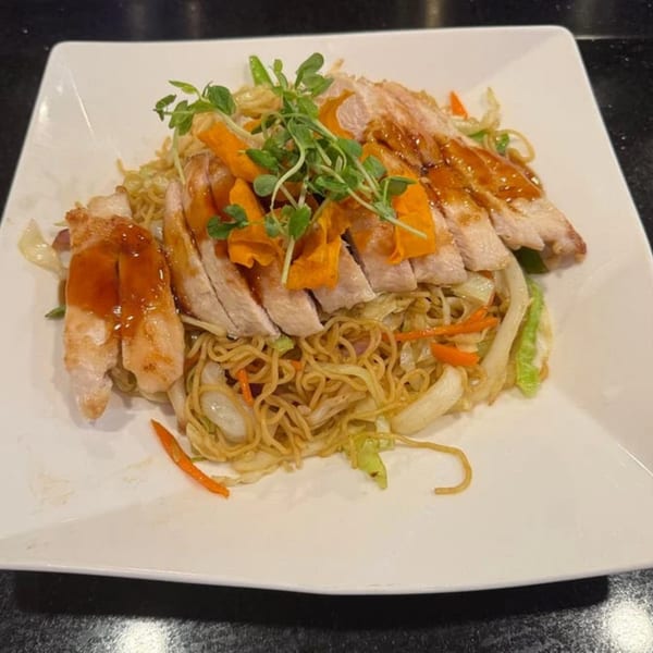 Saga Fusion's chicken teriyaki with noodles, carrots, cabbage, and microgreens on a white plate.